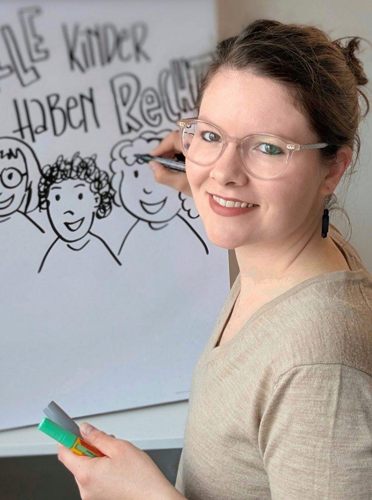 Porträt von Anna Lena Wollny stehend vor einem großen Papier, auf das sie zeichnet und schreibt